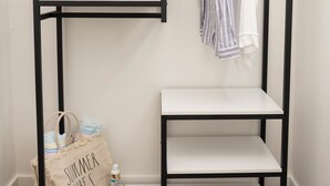 A black metal wardrobe with multiple shelves, a hanging rack, and a small table. - Endless Dunes, A Modern Motel (Eastham)