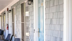 A row of blue doors with a covered porch and chairs outside. - Endless Dunes, A Modern Motel (Eastham)