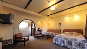 Una habitación de hotel con dos camas, una zona de estar con sillas y una kitchenette.