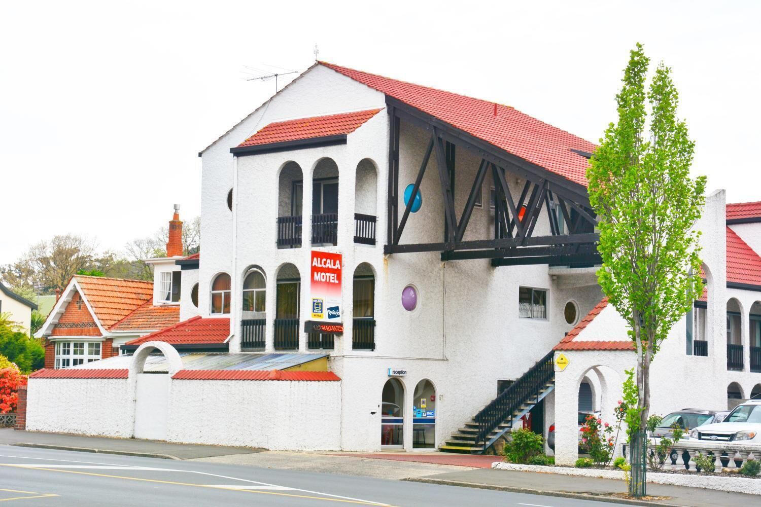 A white building with a red roof, a sign for 'Alcalá Motel', and a staircase leading to the entrance.