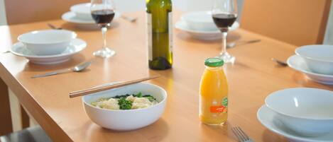 Una mesa de comedor con cuencos, palillos, una botella de jugo de naranja y copas de vino.