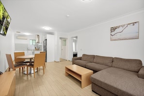 A modern living room with a brown sofa, a wooden coffee table, and a dining area with chairs and a table. - Sunnybank Star Hotel & Apartments (Eight Mile Plains)