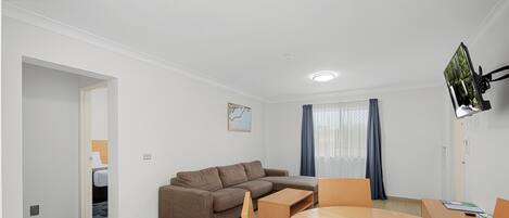 A modern living room with a brown sectional sofa, a wooden dining table with chairs, and a flat-screen TV mounted on the wall.