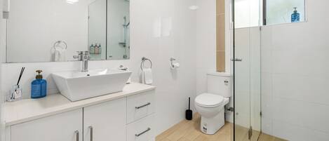 A modern bathroom with a white sink, mirror, and toilet.