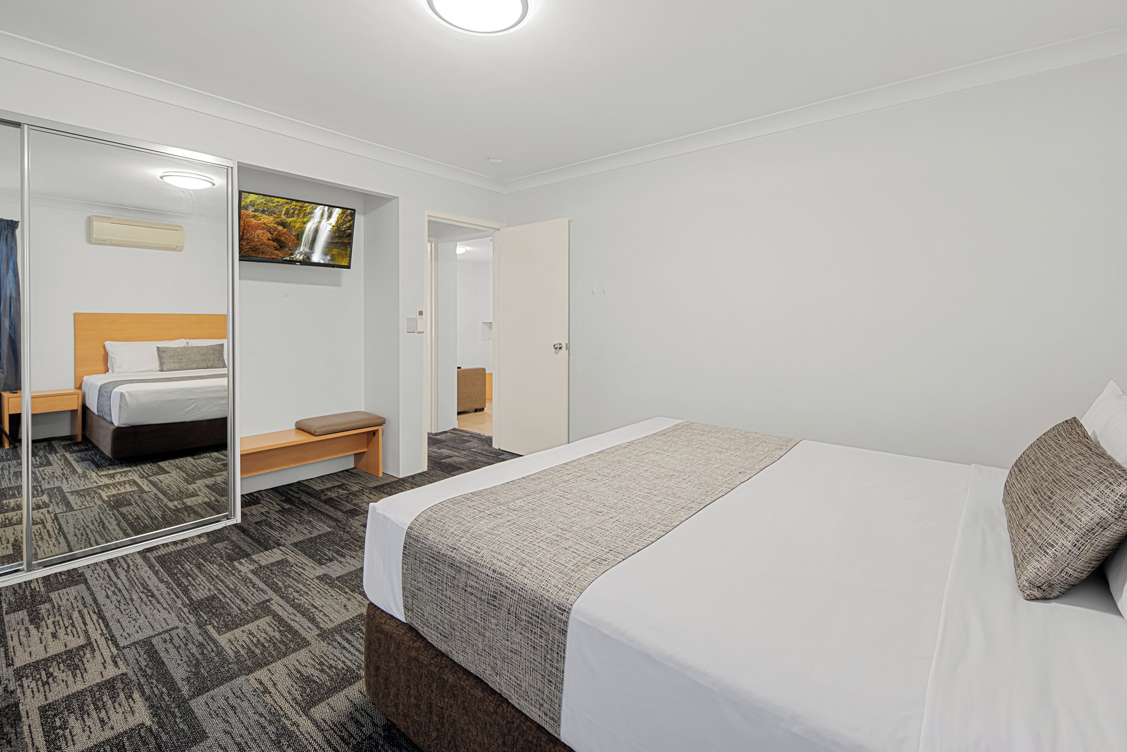 A hotel room with a bed, a bench, a TV, and a mirror.