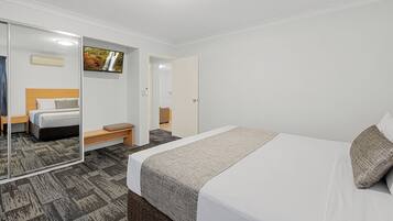 A hotel room with a bed, a bench, a TV, and a mirror.