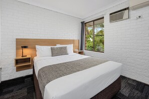 A hotel room with a large bed, a nightstand, a lamp, and a window with a view of greenery. - Sunnybank Star Hotel & Apartments (Eight Mile Plains)