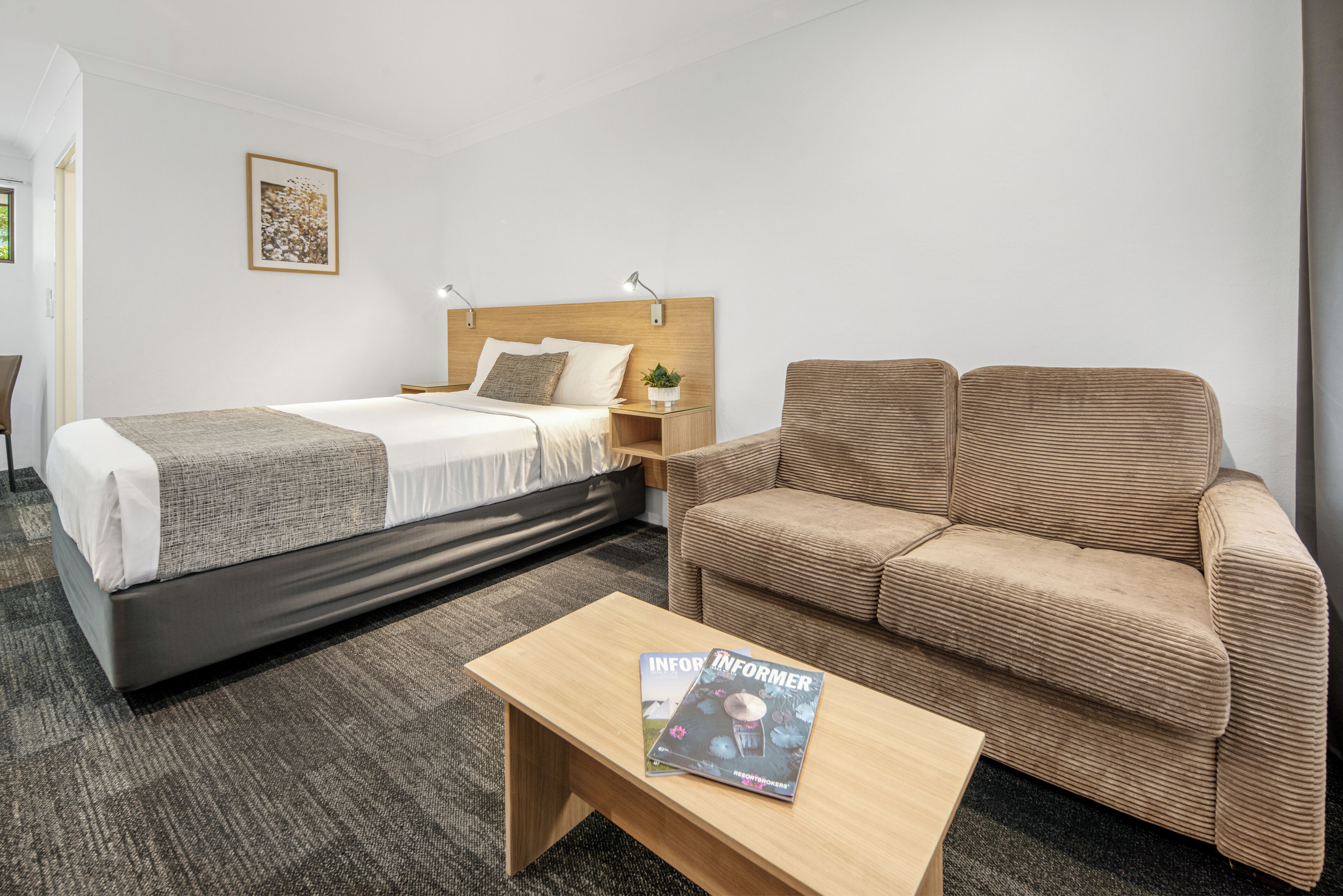 Una habitación de hotel con cama, sofá, mesita de noche, lámpara y una revista sobre la mesa.