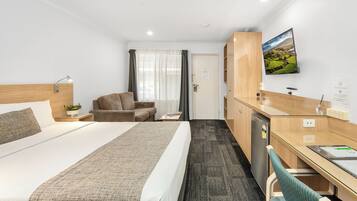 Ett hotellrum med en säng, ett skrivbord, en stol, ett litet bord, en tv och ett fönster med gardiner.