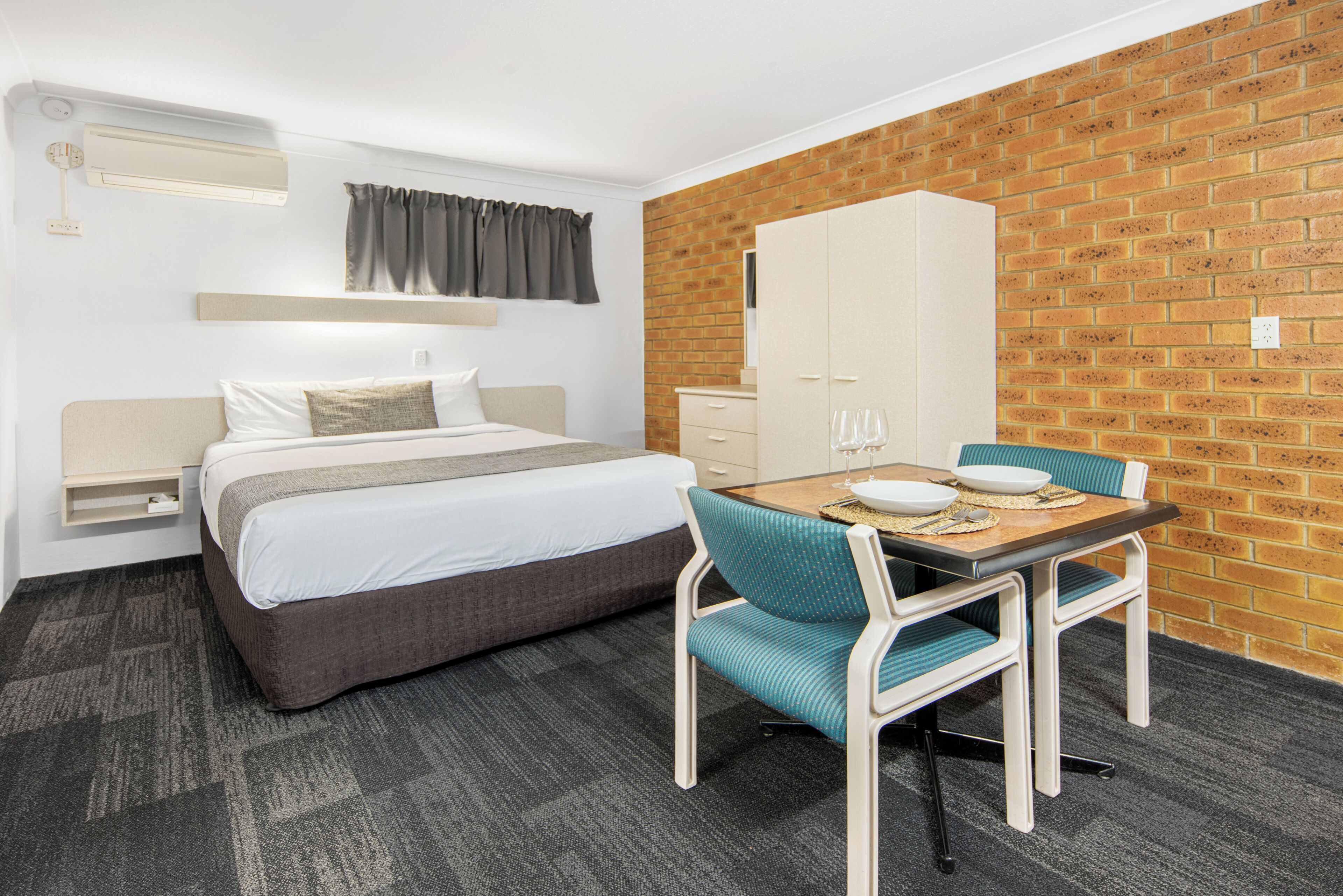 Une chambre d’hôtel avec un lit, une table et des chaises, une armoire et un mur en briques.