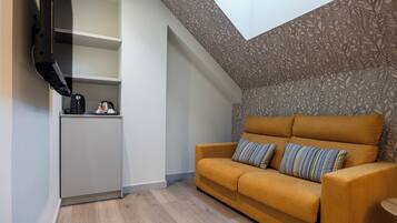 A compact living space with a sofa, a small kitchenette, and a sloped ceiling with a skylight.