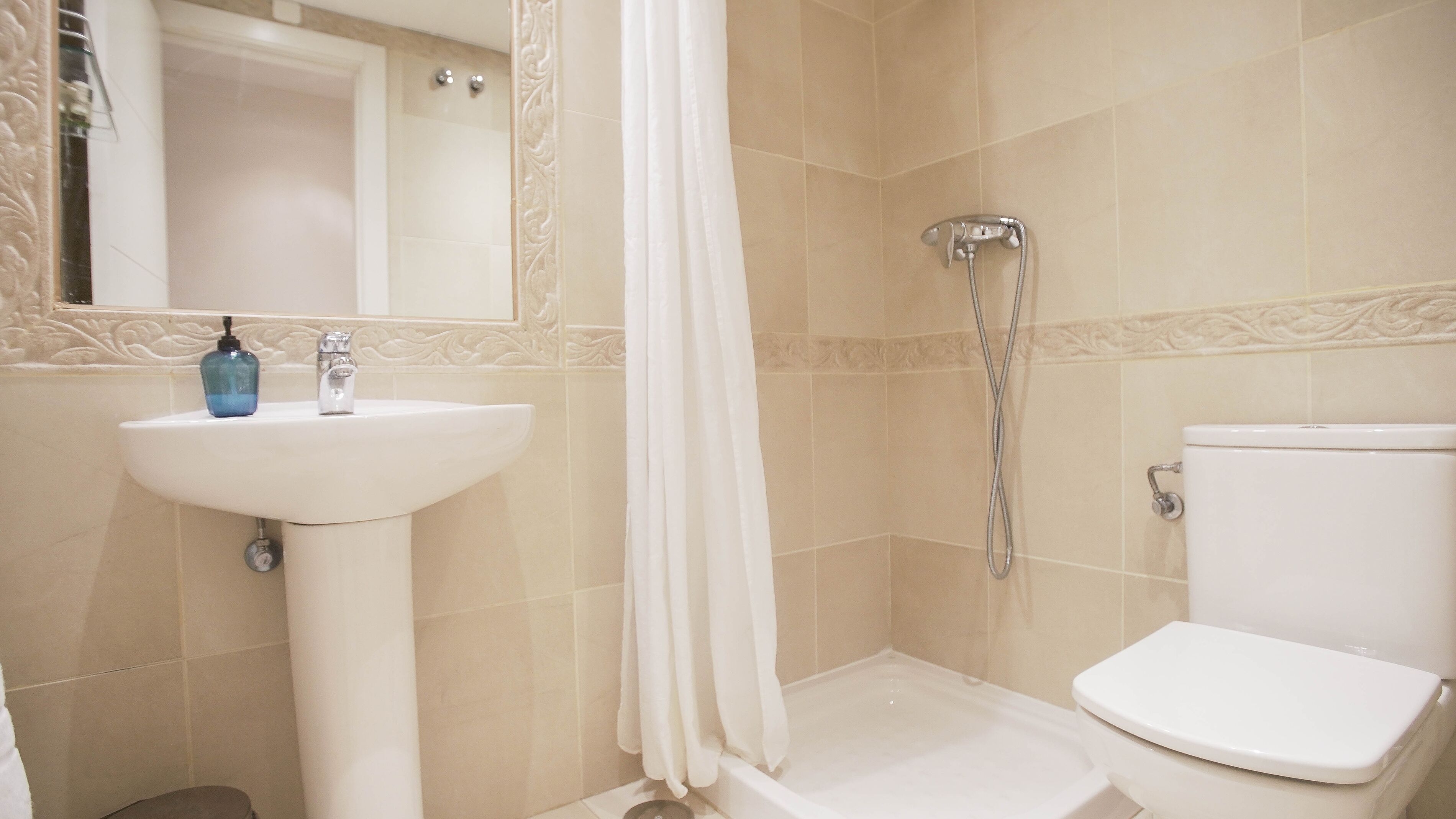 A bathroom with a sink, toilet, shower, and a mirror.
