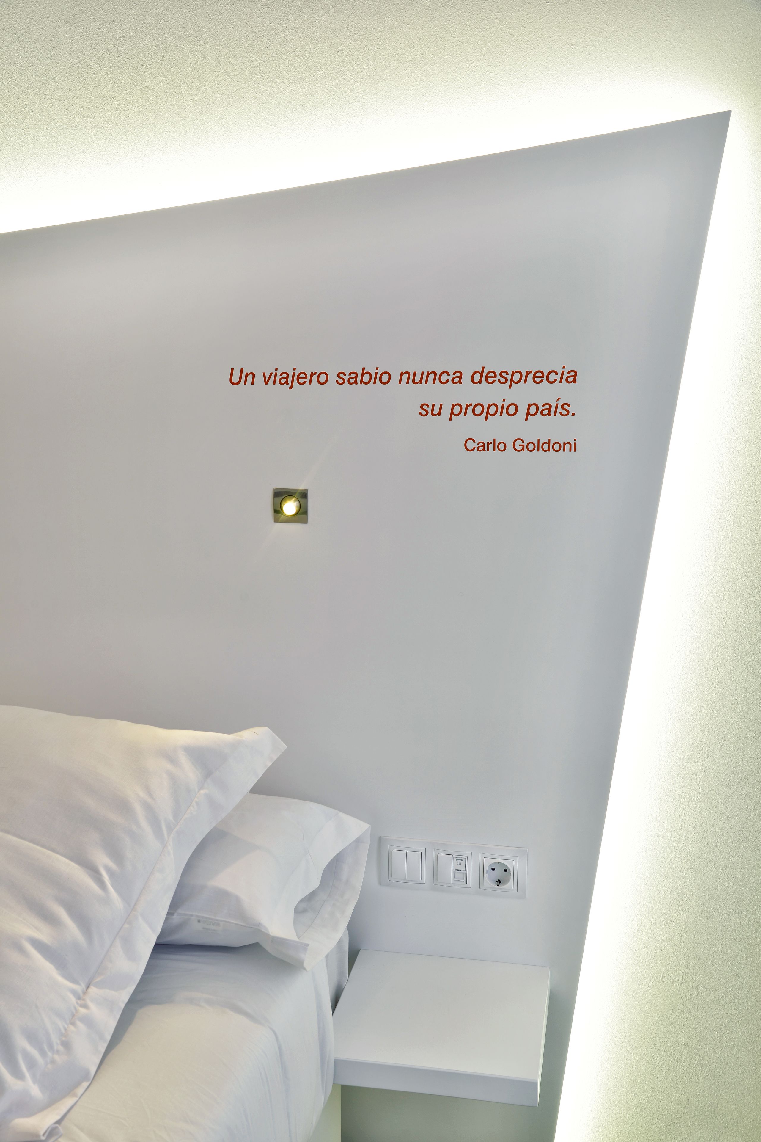 Un dormitorio moderno con una cama blanca, una mesita de noche y una lámpara de pared.