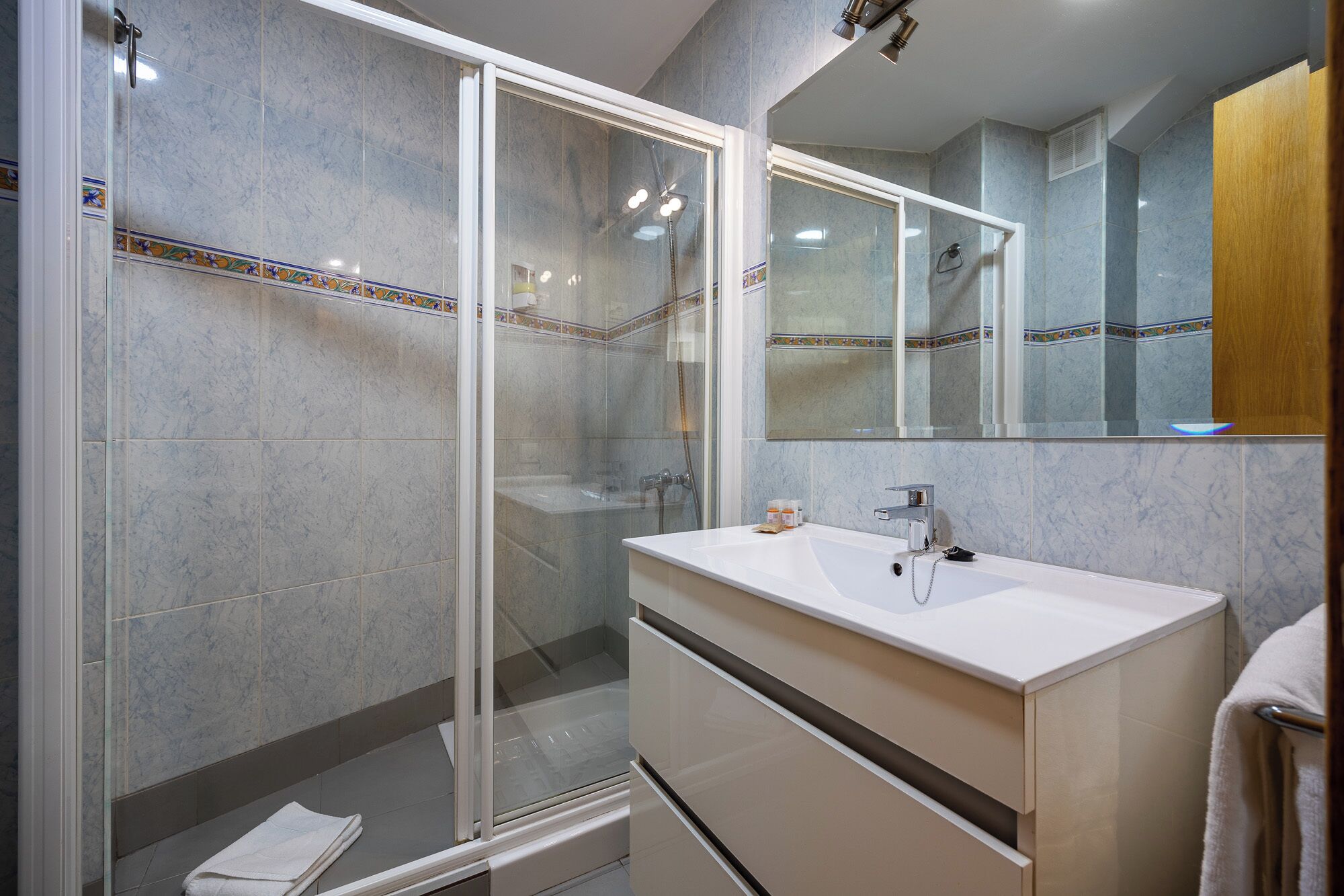 Un baño moderno con ducha envuelta en vidrio, un tocador blanco con espejo y azulejos de mármol.