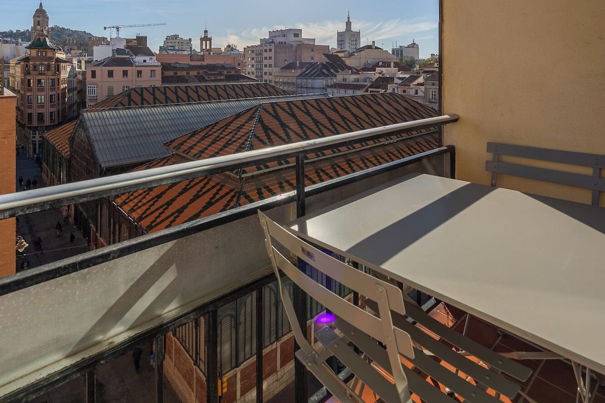 A balcony with a table and chairs, overlooking a cityscape with buildings and a clear sky.