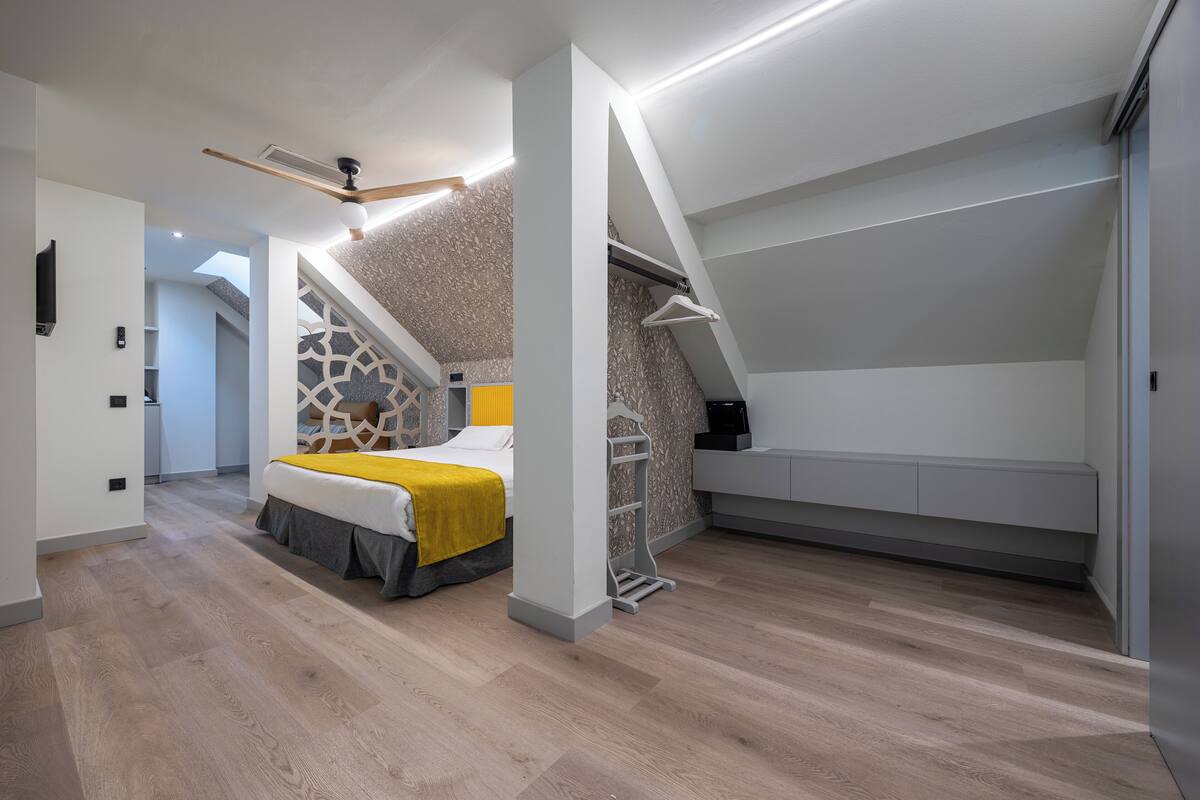 A modern bedroom with a bed, a ceiling fan, a built-in wardrobe, and a sloped ceiling.