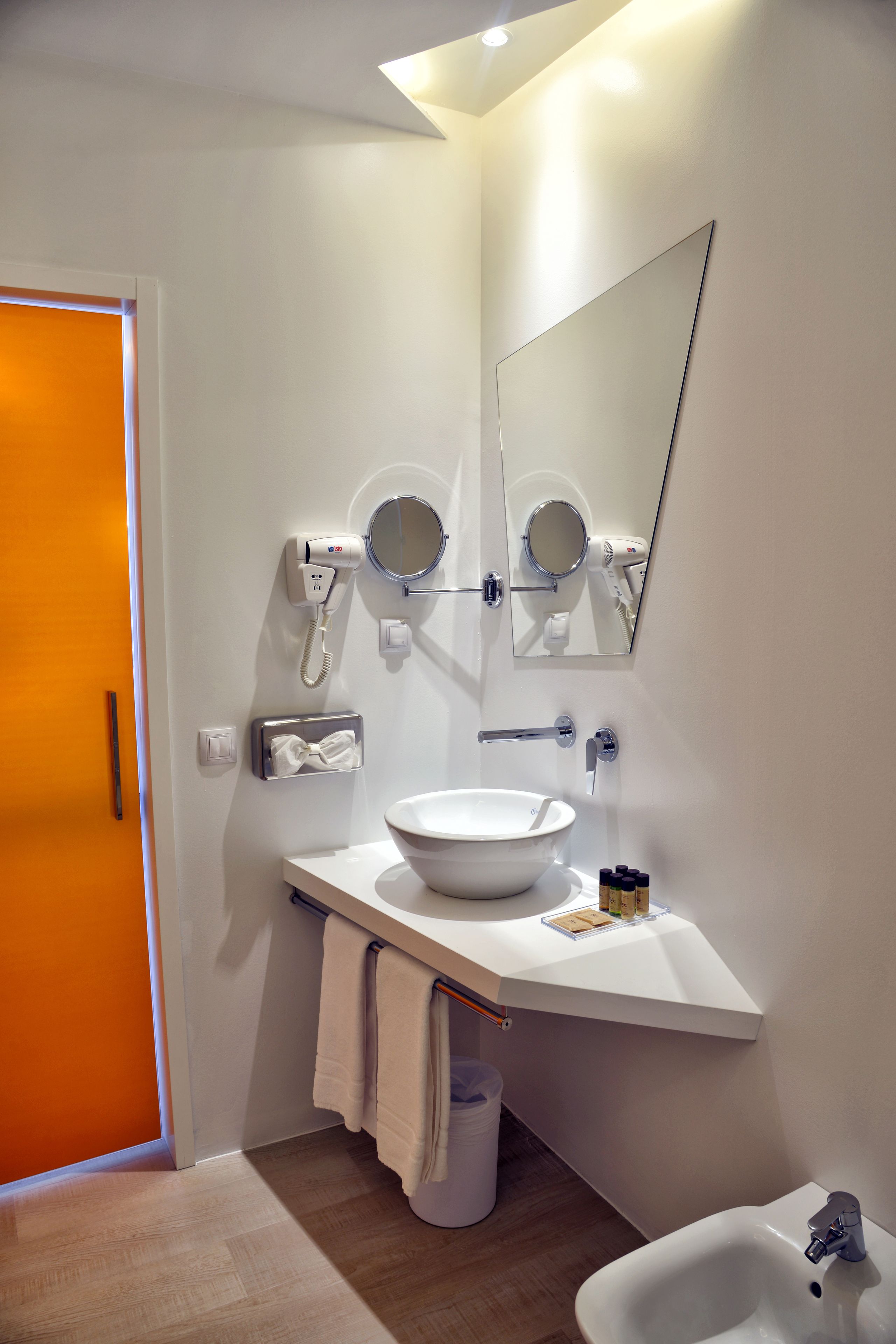 Une salle de bain moderne avec un lavabo blanc, un miroir, un sèche-cheveux et un bidet.