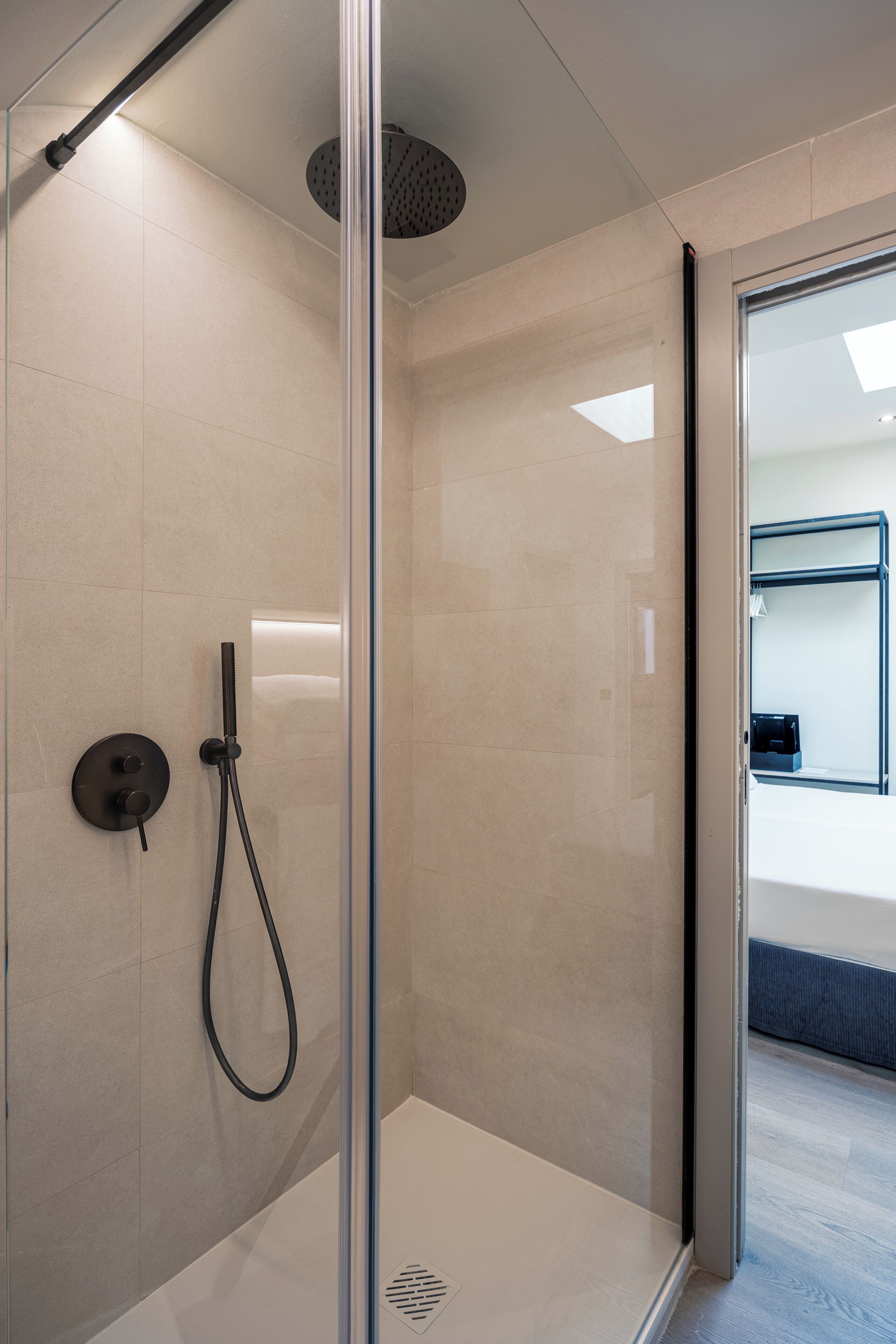 A modern shower with a glass door, a handheld showerhead, and a control panel.