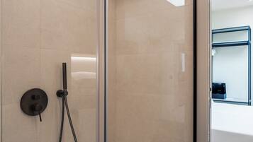 A modern shower with a glass door, a handheld showerhead, and a control panel.