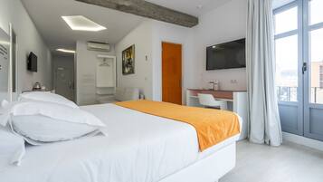 Une chambre d’hôtel avec un grand lit, un plaid orange, un bureau avec une chaise, une télévision et un balcon avec des rideaux.