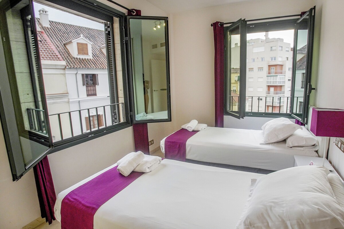 A hotel room with two beds, a window, and a mirror.