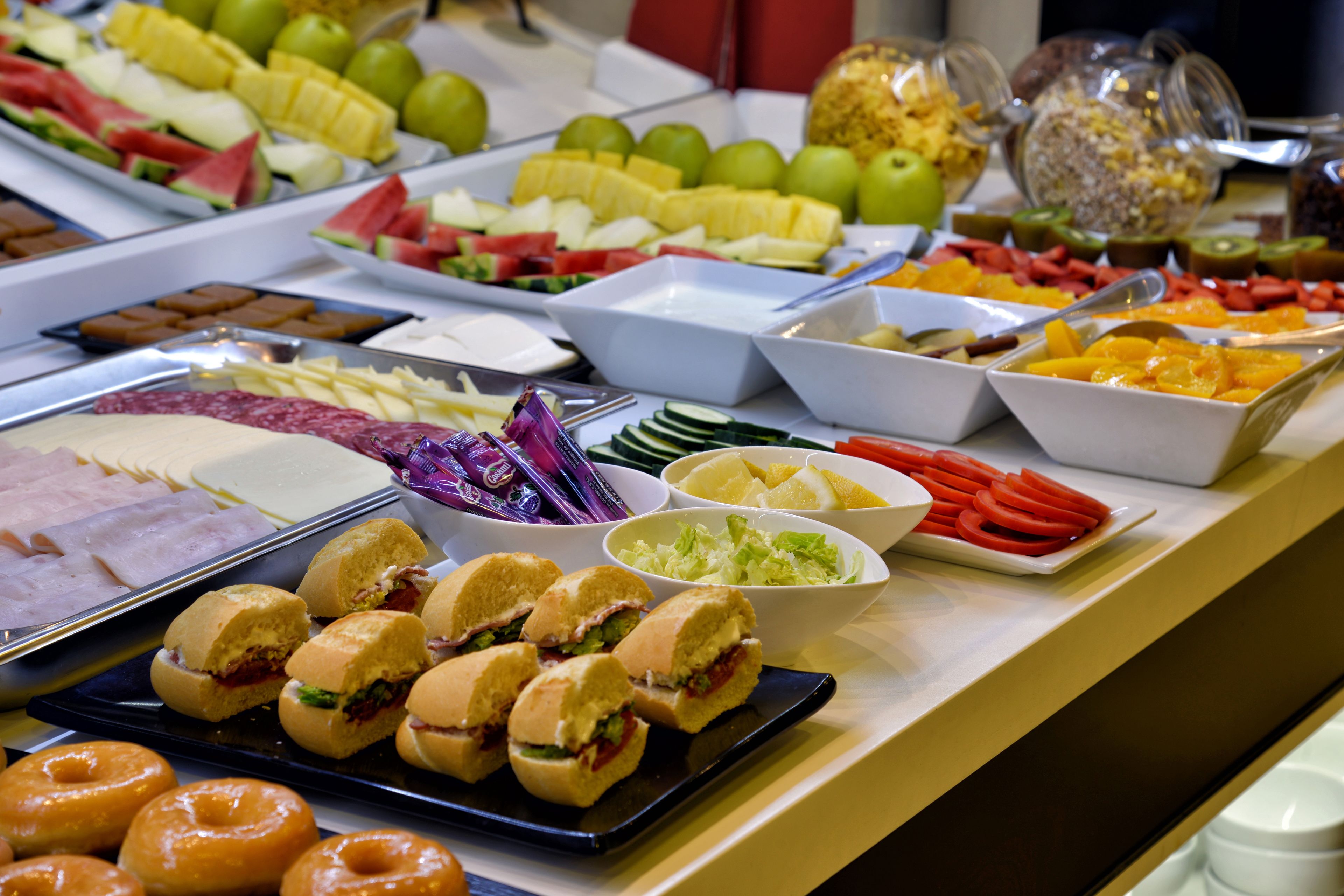 Un bufé con diversas opciones de comida, incluyendo frutas, verduras, sándwiches y pasteles.