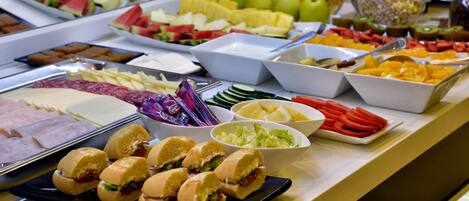 Un bufé con diversas opciones de comida, incluyendo frutas, verduras, sándwiches y pasteles.