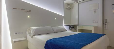 A modern hotel room with a bed, bedside table, and a mirror above the dresser.