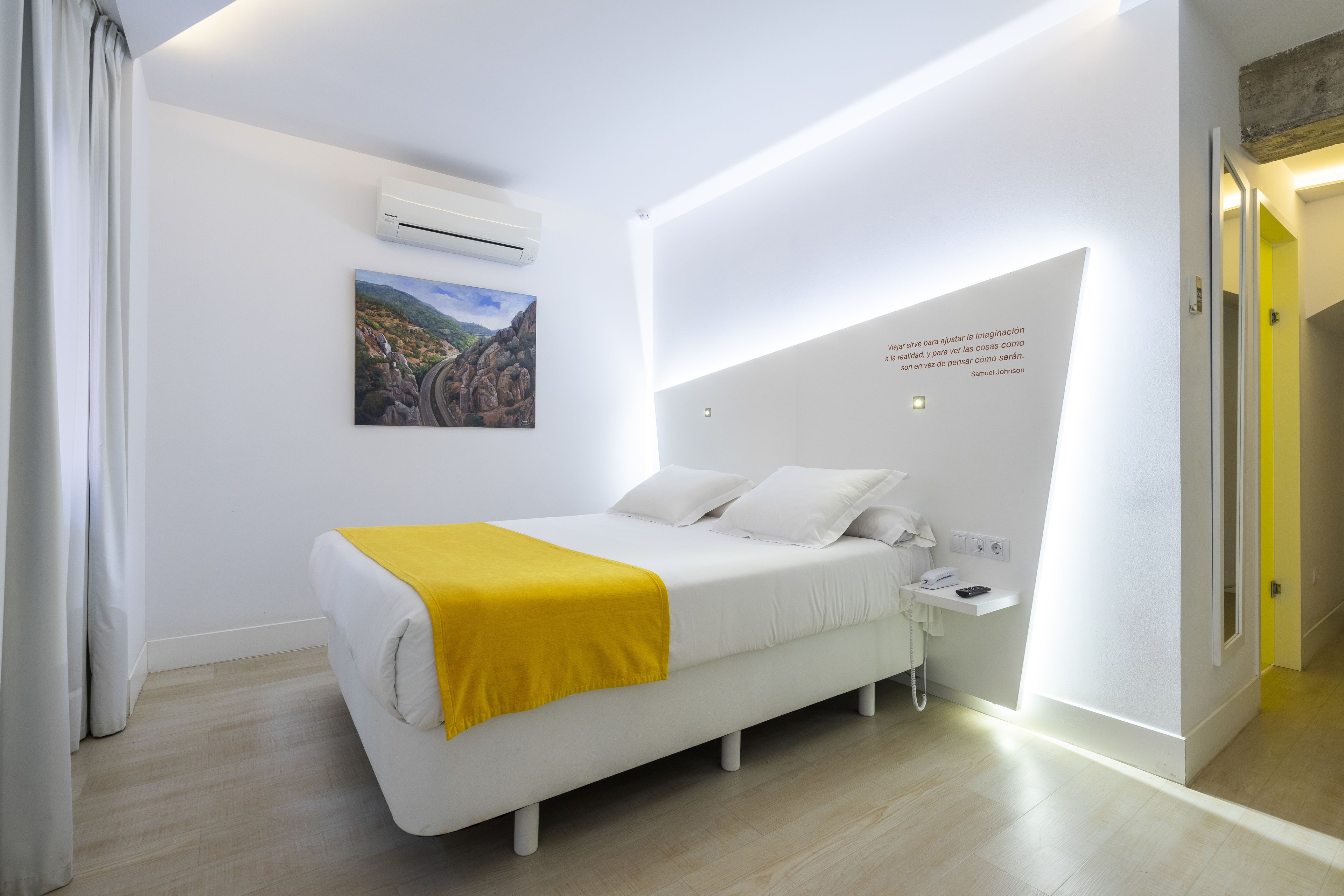 Una habitación de hotel moderna con cama, un cuadro, un equipo de aire acondicionado y una cita en la pared.