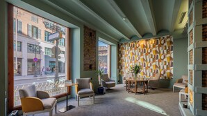 A cozy interior with a seating area, a patterned wall, and large windows overlooking a street.