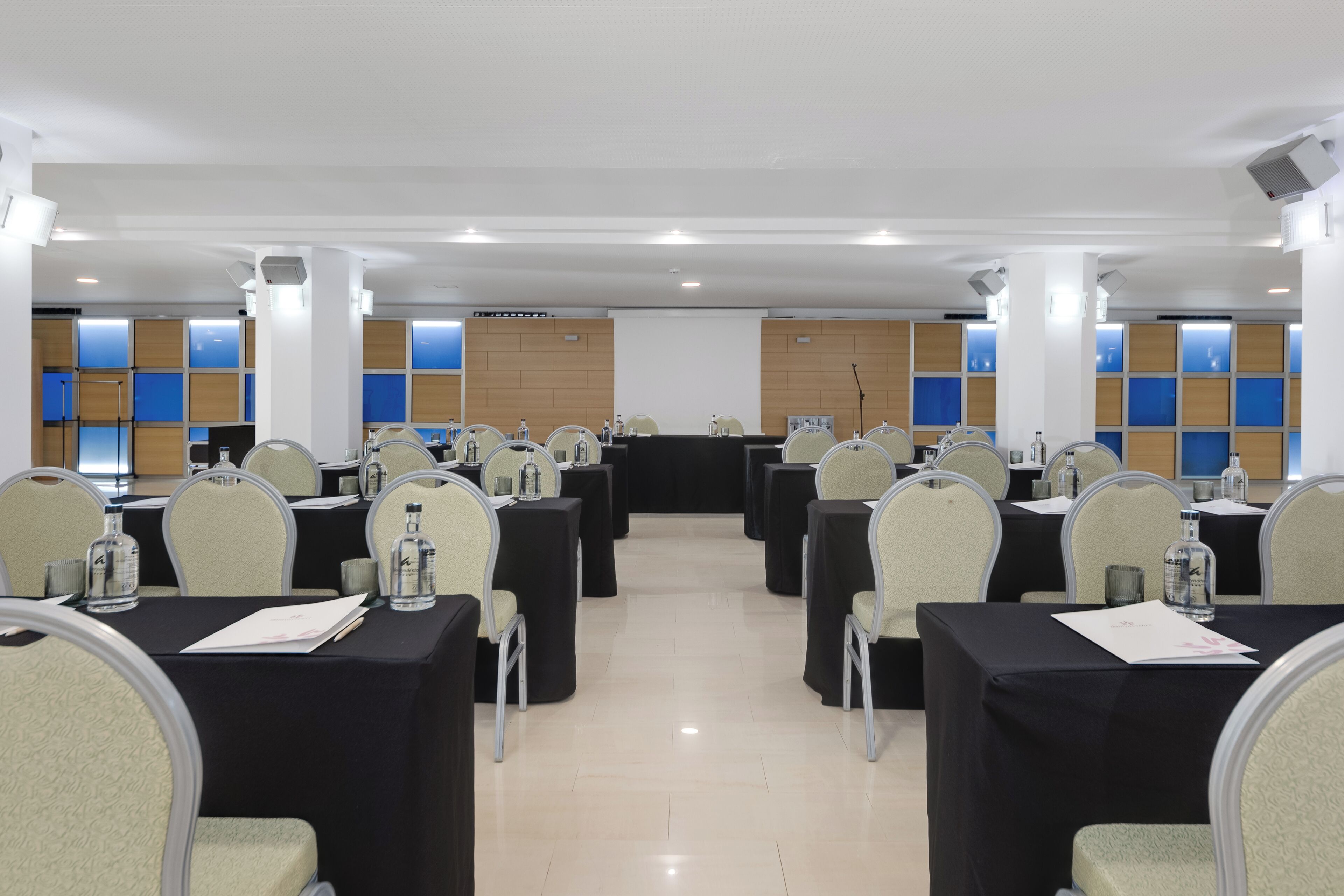 A conference room with rows of tables and chairs, a podium, and a projection screen.
