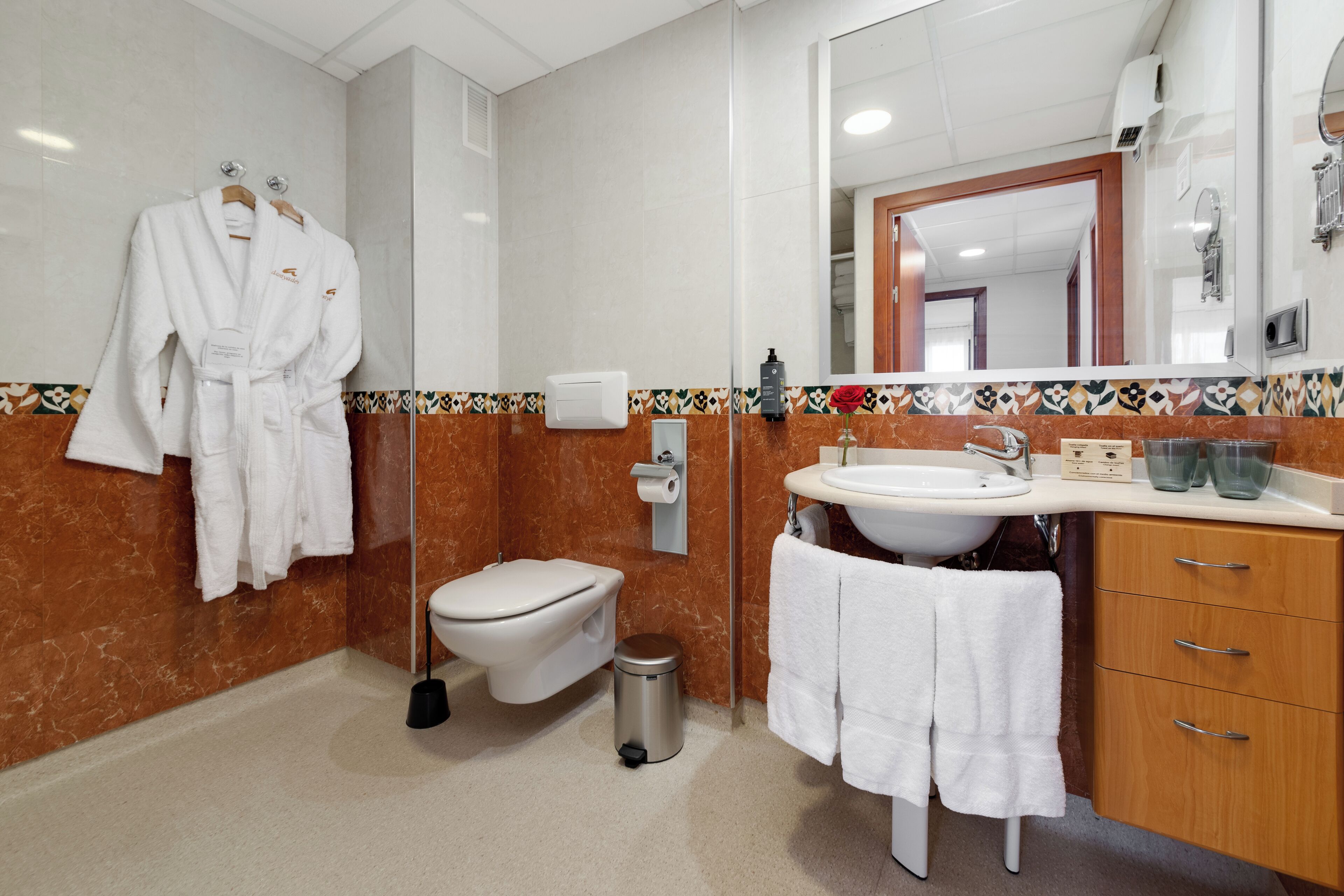 A bathroom with a toilet, sink, and mirror. There are white towels and a trash can.