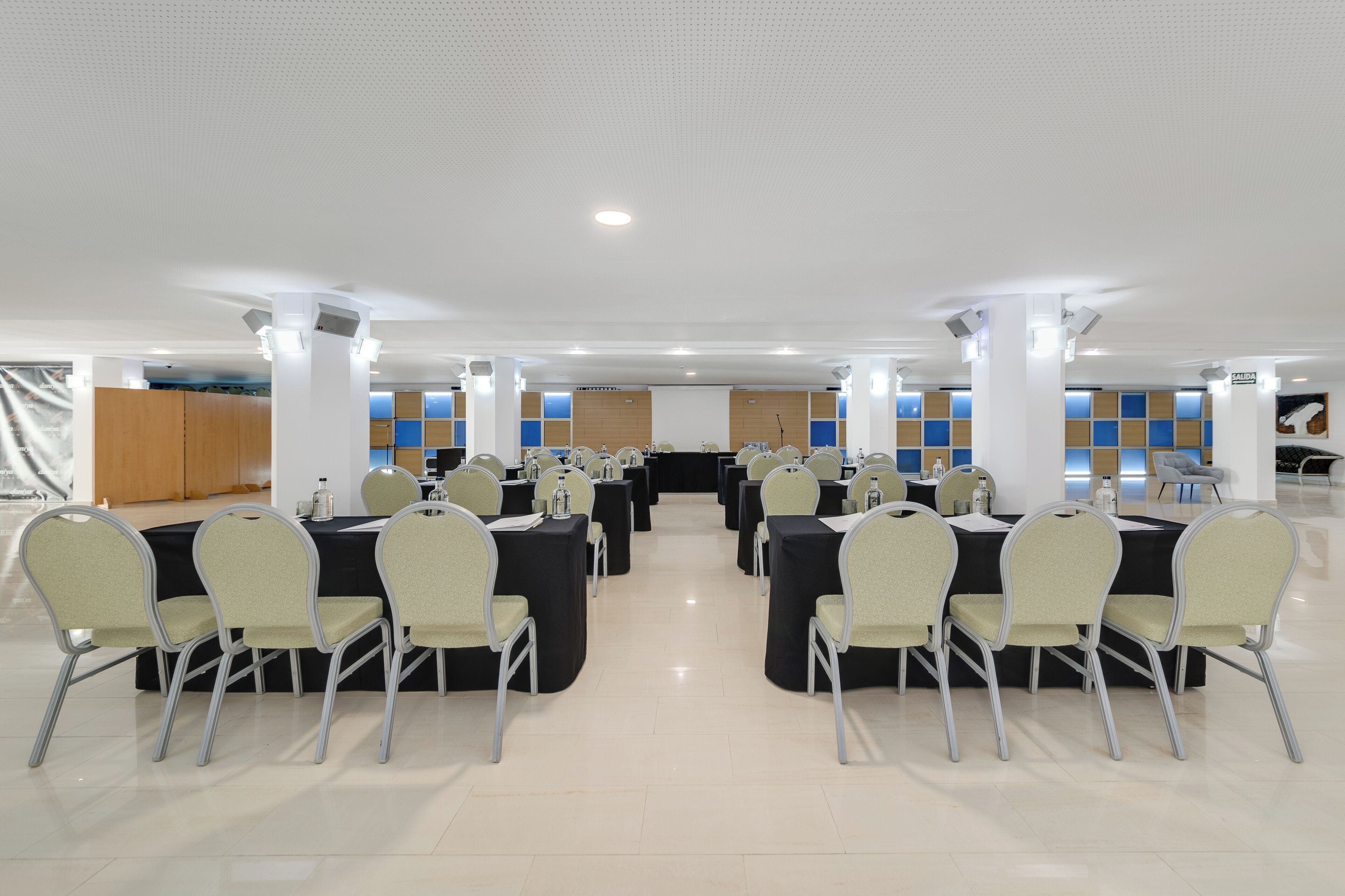 A conference room with multiple tables and chairs, white pillars, and a tiled floor.
