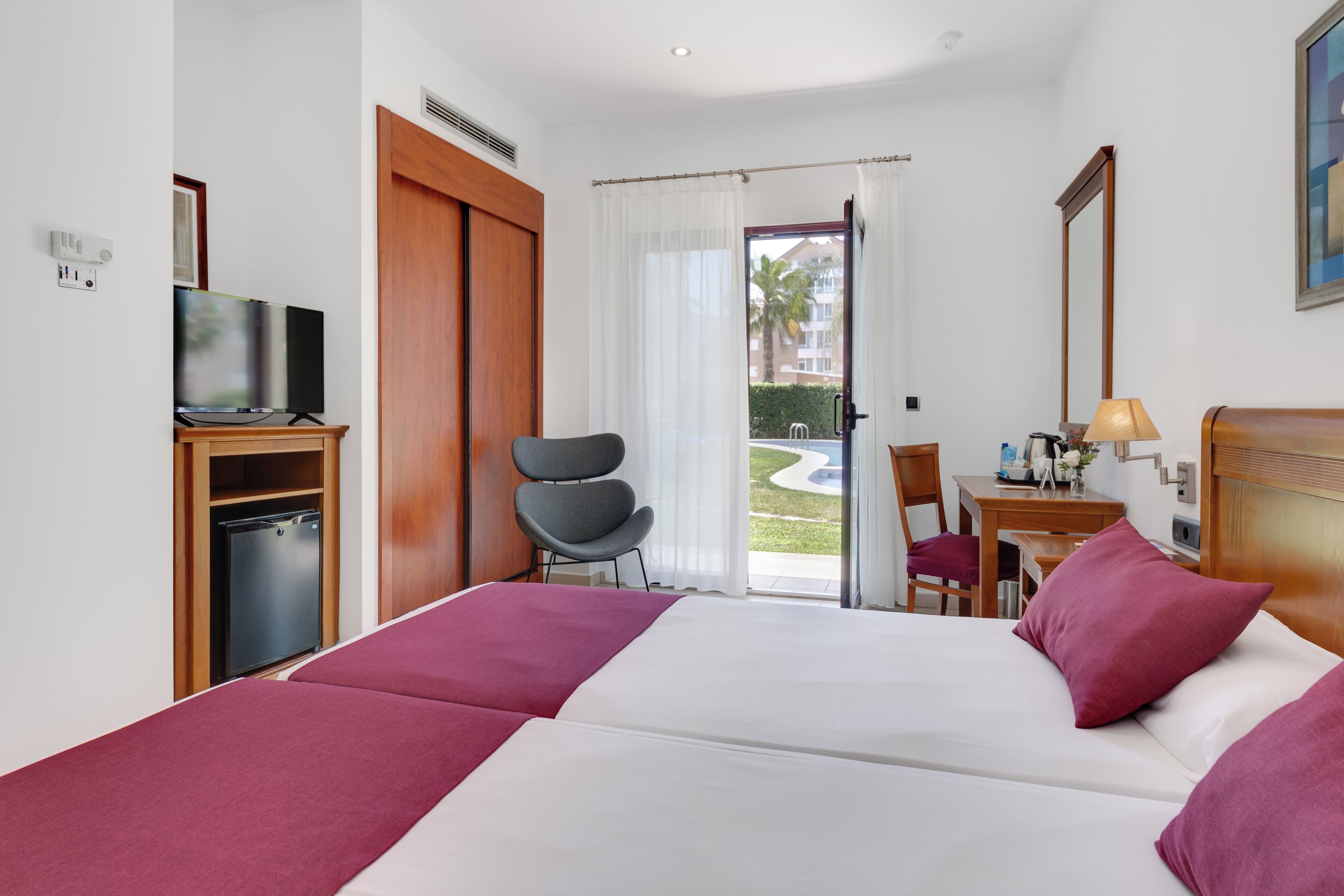 A hotel room with a bed, a desk, a chair, a television, and a view of the outdoors.