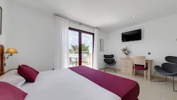 Habitación de hotel con cama, escritorio, dos sillas, televisor y balcón con vista.