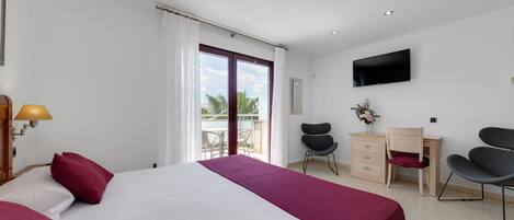 A hotel room with a bed, desk, two chairs, a TV, and a balcony with a view.