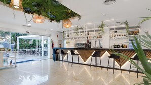 Zona de bar moderna con suelo de mármol pulido, taburetes y una variedad de botellas y copas en estanterías.