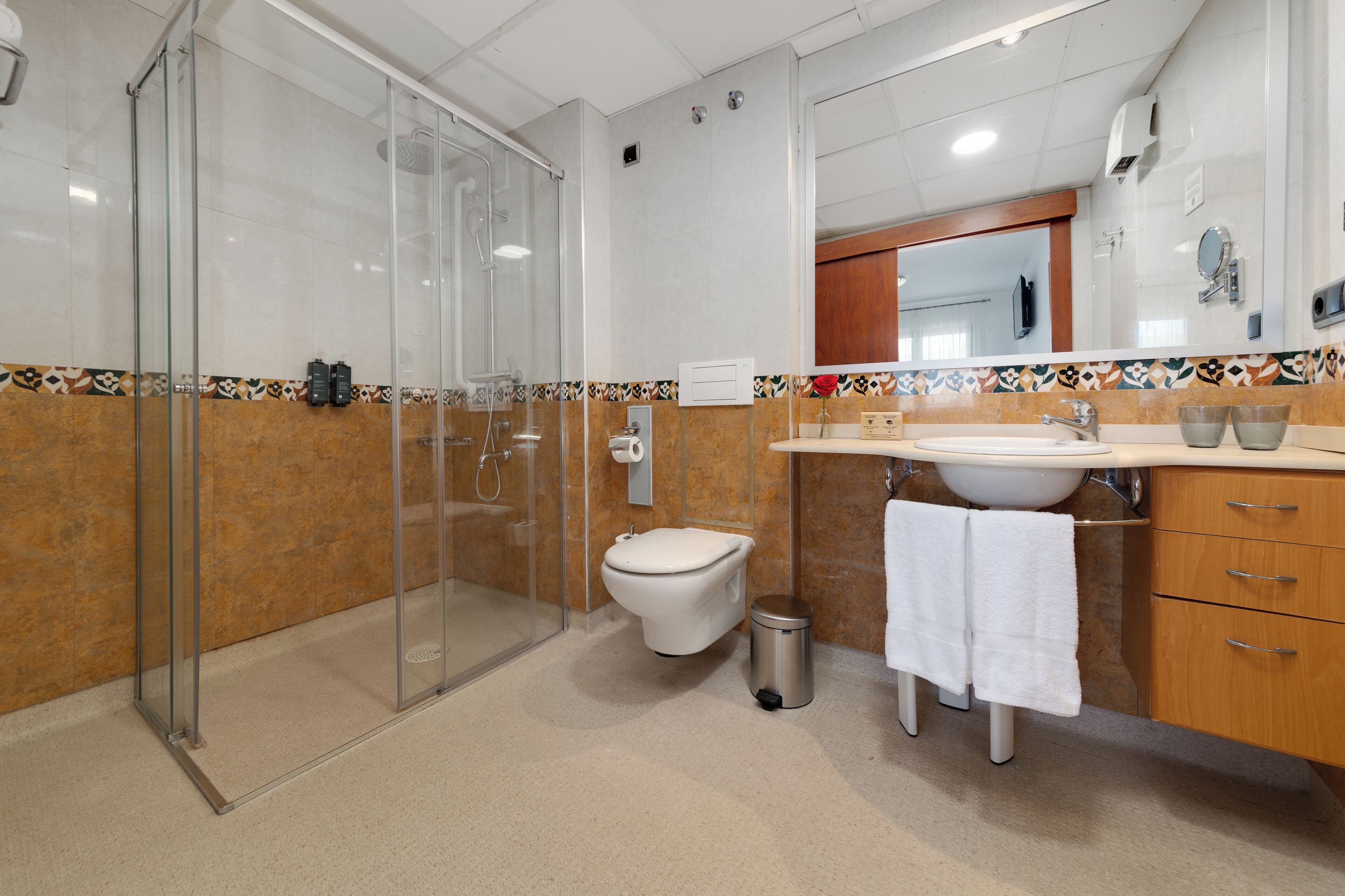 Une salle de bain moderne avec une douche à parois de verre, des toilettes, un lavabo avec un miroir et une poubelle.