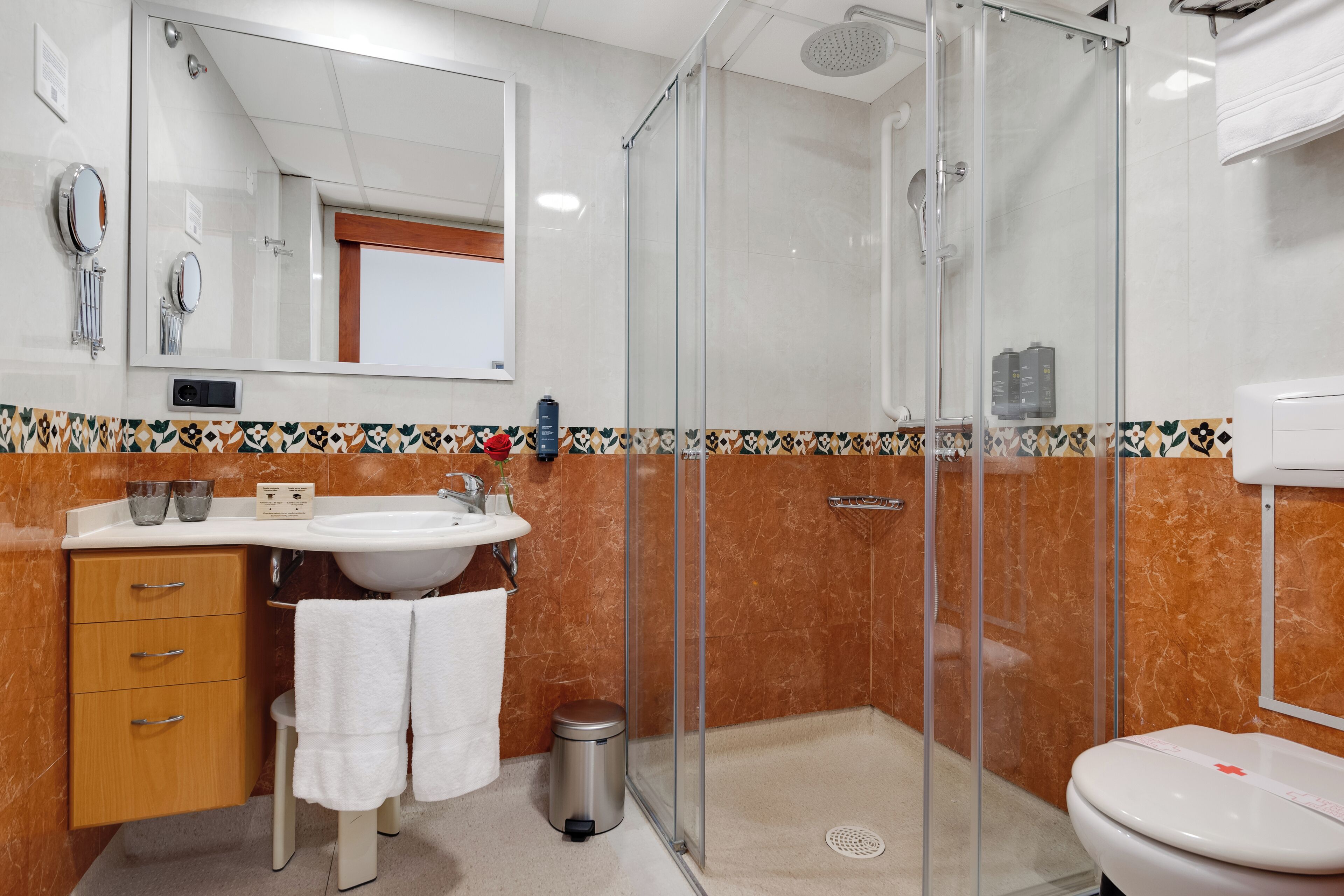 Un baño moderno con ducha de vidrio, un lavamanos con espejo y un inodoro.