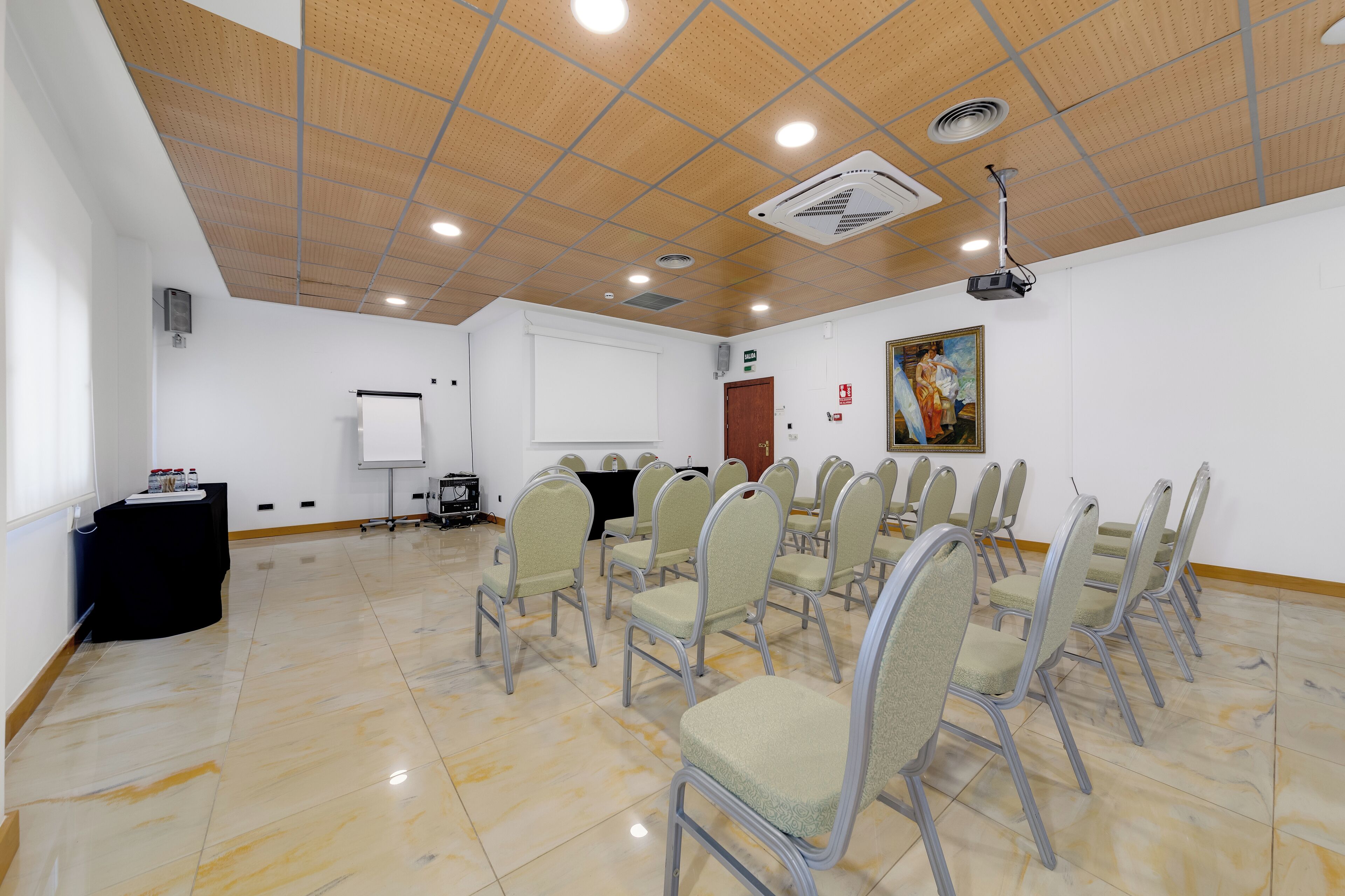 Un salón de conferencias con una pizarra, un proyector y filas de sillas.