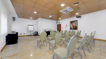 Un salón de conferencias con una pizarra, un proyector y filas de sillas.