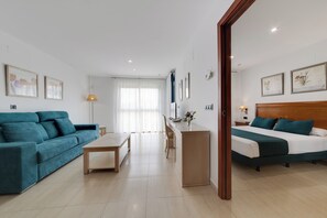 A modern hotel room with a sofa, a desk, a bed, and a view of the city.