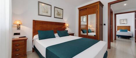 A hotel room with a large bed, wooden headboard, two bedside tables with lamps, a wardrobe, and a mirror.