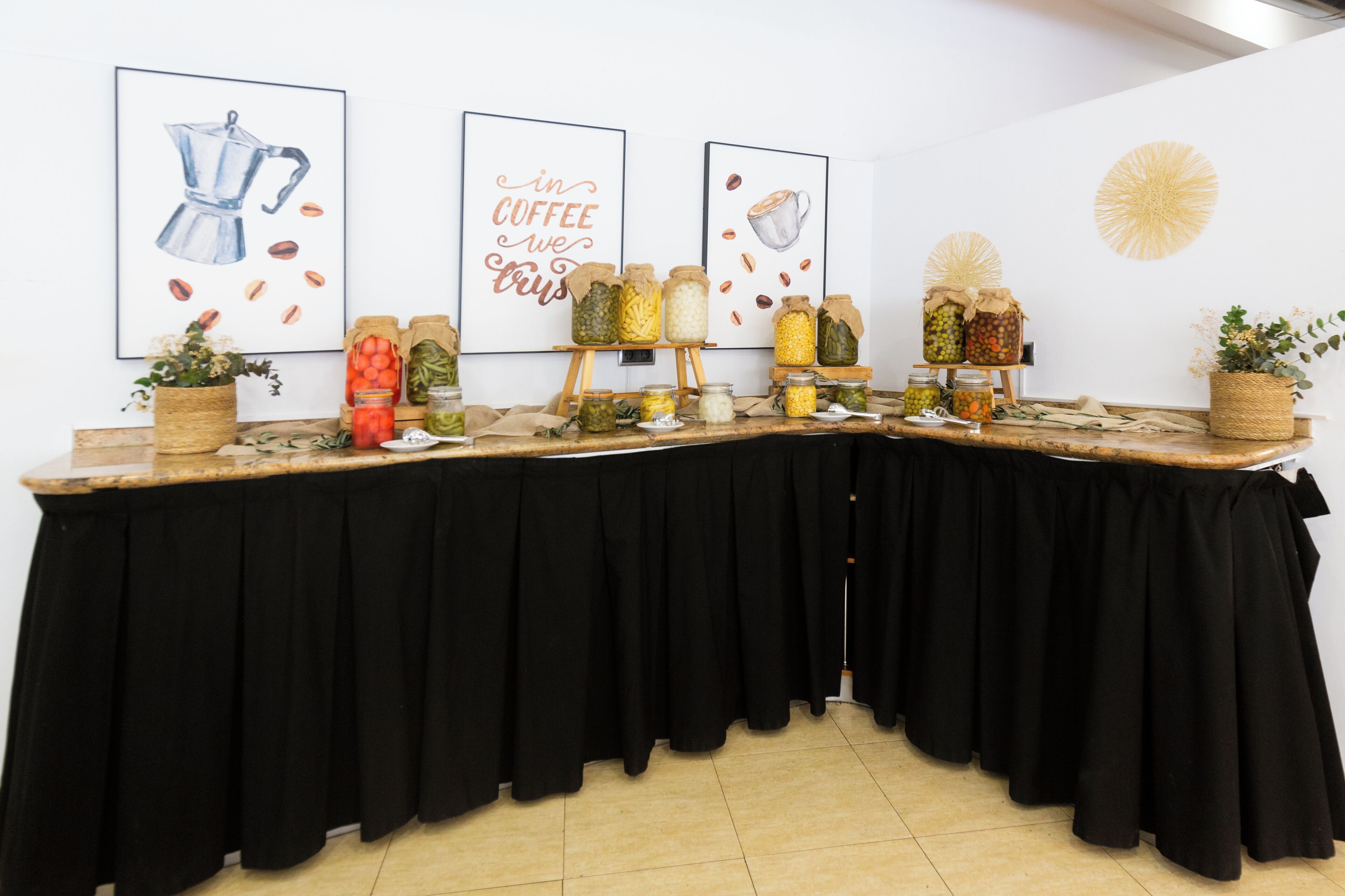 A long table with black tablecloths, decorated with jars of pickled vegetables, a coffee pot illustration, and a coffee cup illustration.