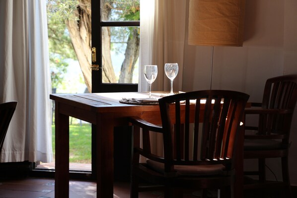 A dining table with two wine glasses, a lamp, and chairs in a room with a view of trees and a door. - Hotel Cerro de Hijar (Tolox)