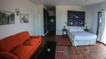 Une chambre d’hôtel comprenant un lit, un canapé, une table basse, un téléviseur fixé au mur et un ventilateur de plafond.