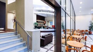 A hotel lobby with a staircase, a bar area, and a seating area with tables and chairs. - The Athens Mirabello (Athens)