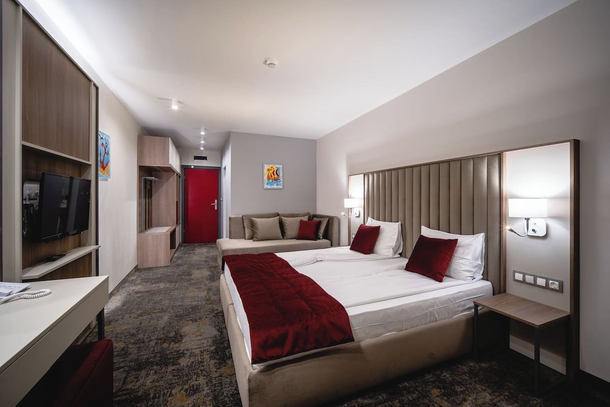 A hotel room with two beds, a TV, a desk, and a red door.