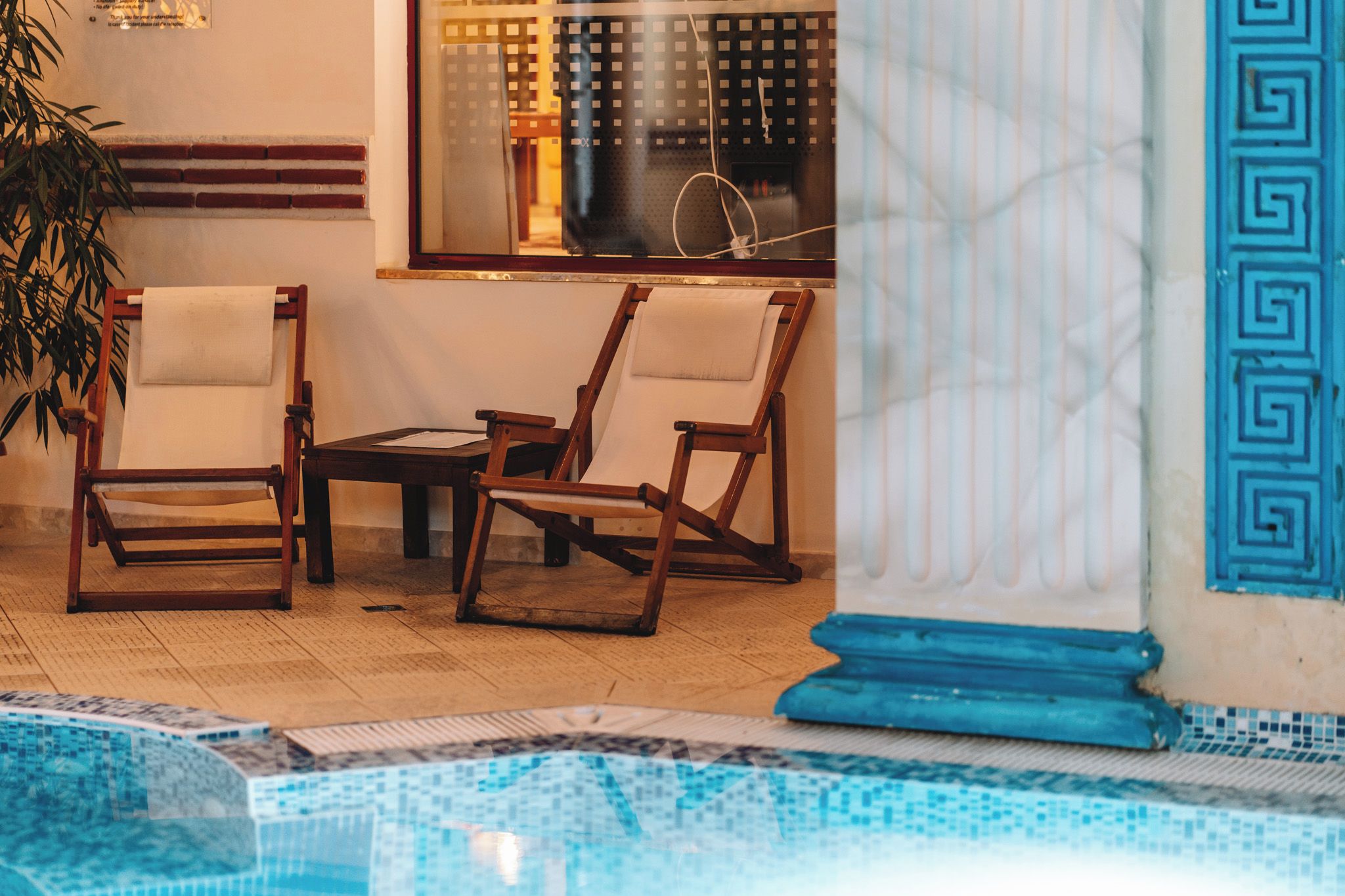 A pool area with wooden chairs and a tiled floor.