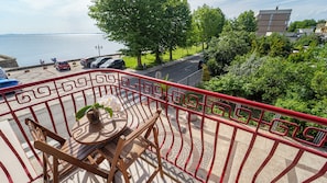 A balcony with a red railing overlooking a body of water, a small table with a potted orchid, and a view of parked cars and greenery. - Saint George Hotel & Spa (Pomorie)
